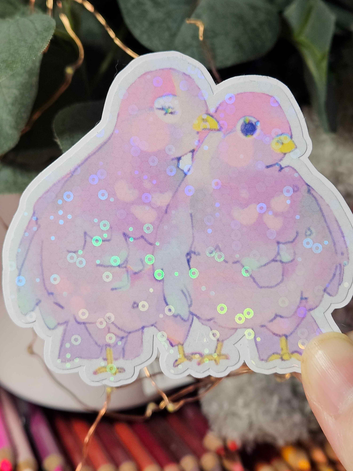 Close-up of Wander Pigeons holographic sticker showing glitter shimmer and hand-drawn feather detail